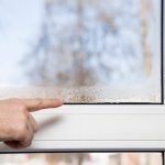Man's hand pointing to the window glass humidity. Room airing problem.